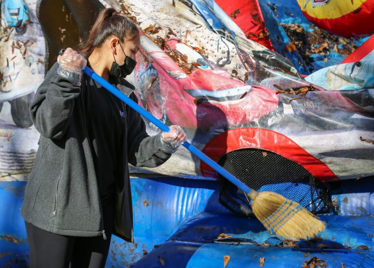 A Faulkner student brushes leaves and debris off an outside inflatable play house at Mercy House on MLK Day, January 18, 2021.