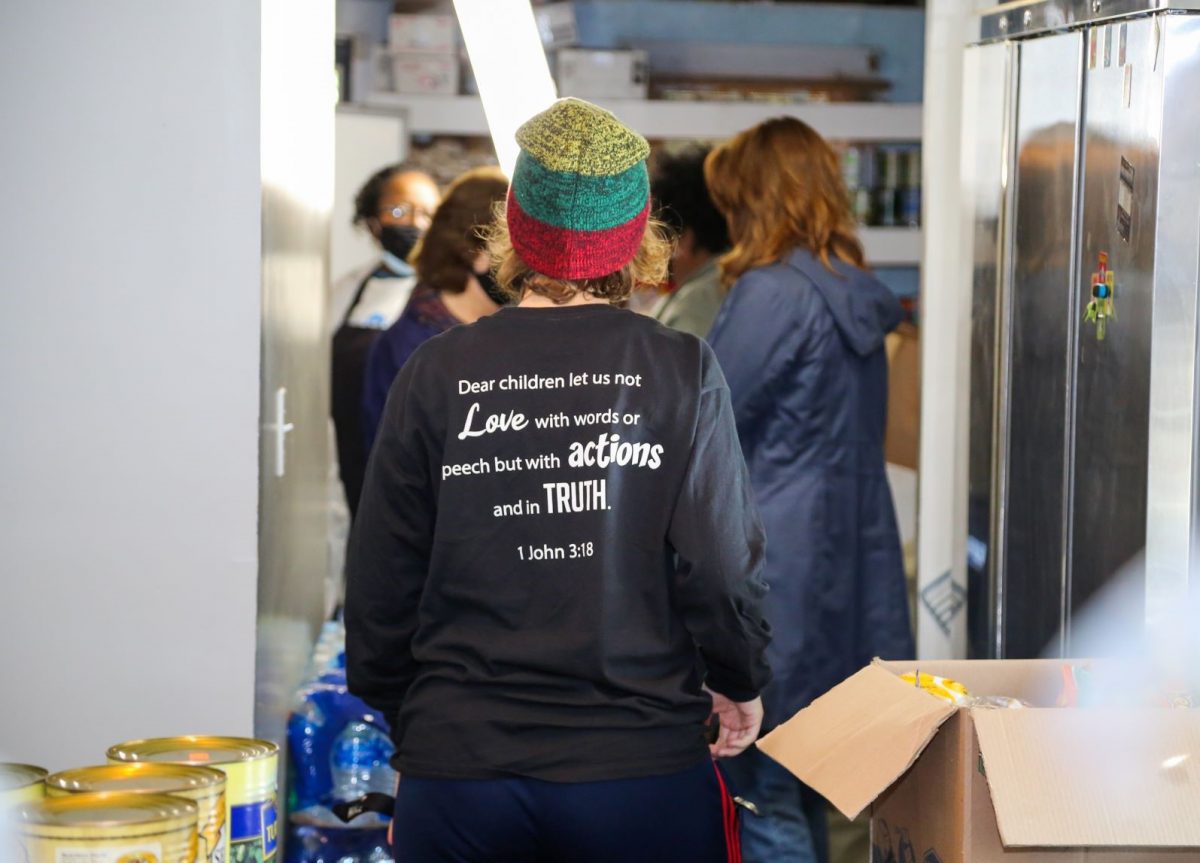 A student volunteer helps in the Mercy House kitchen. On the back of her Faulkner volunteer shirt is written the verse from 1 John 3:18, "Dear children let us not love with words or speech but with actions and in truth."