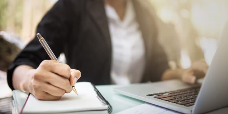 Student takes notes while studying on laptop