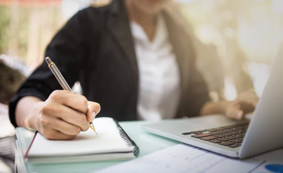 Student takes notes while studying on laptop