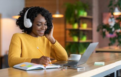 Student wearing yellow sweater smiling while studying on laptop