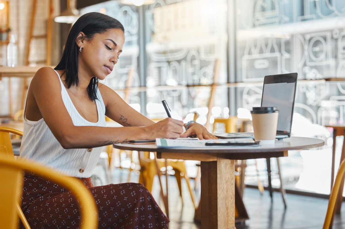 Student with laptop takes notes in coffee shop