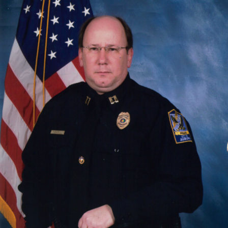 Tommy Carswell poses in front of the United States of America flag wearing his police captain uniform.