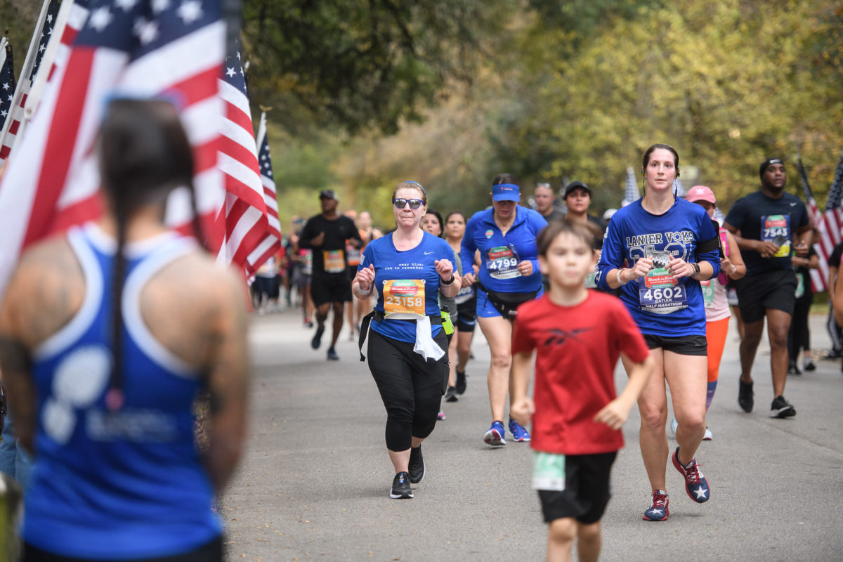 Laurie Brookshire, center runs with a large group alongside a line of people holding American flags. 