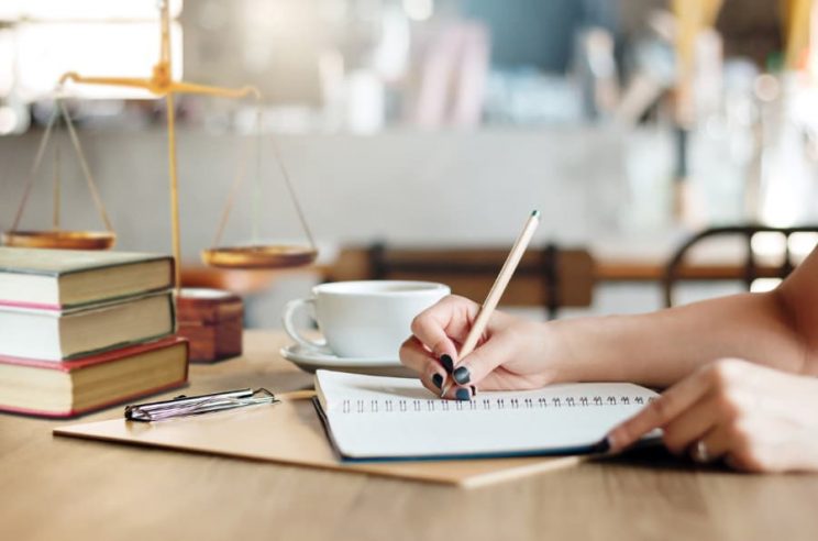 Woman writes on paper with scales of justice in background