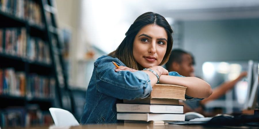 A-student-with-a-stack-of-books-in-a-library A student with a stack of books in a library