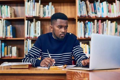 Young Man in Library Studying on Laptop