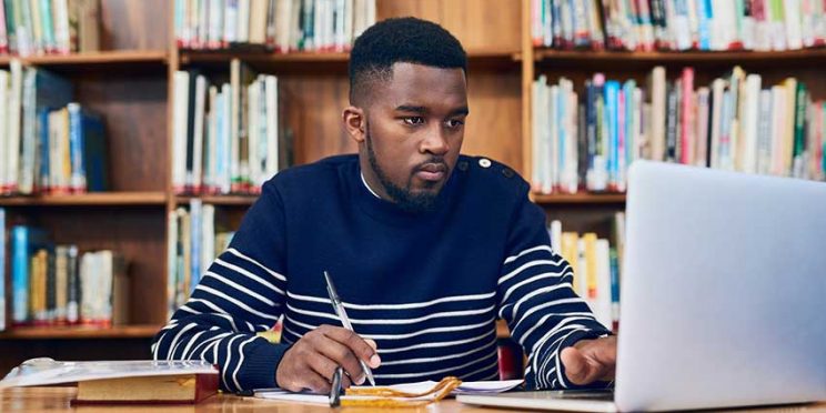 Young Man in Library Studying on Laptop