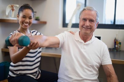Therapist helps elderly patient with physical therapy exercises using a dumbbell