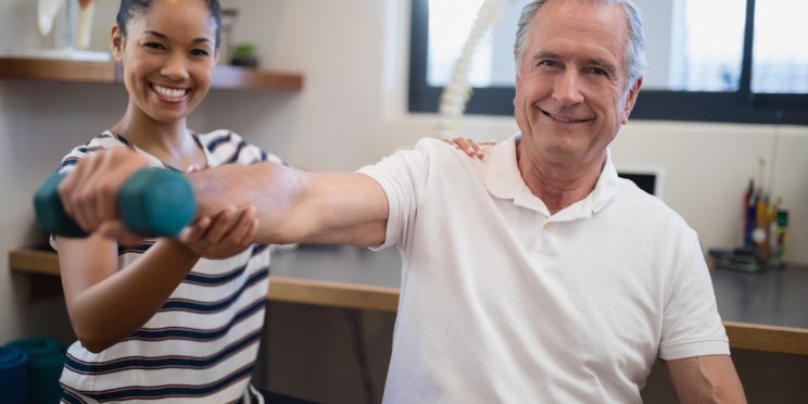 Therapist helps elderly patient with physical therapy exercises using a dumbbell