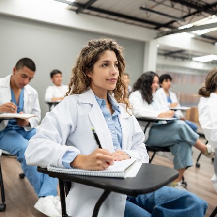 Group of medical students sitting at desks in classroom and taking notes