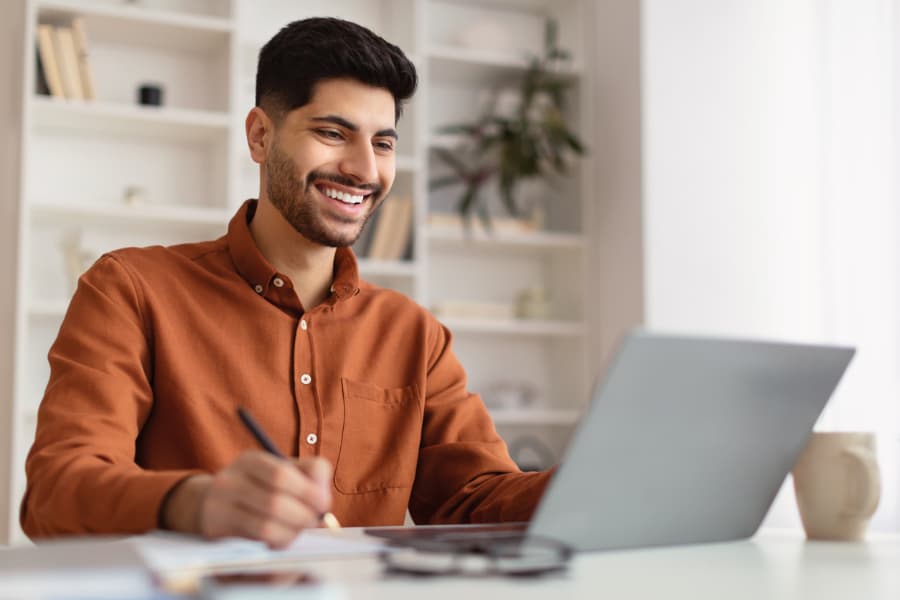 Smiling man working on laptop and taking notes
