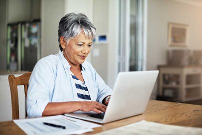 Older Woman Sitting at Table Typing on Laptop