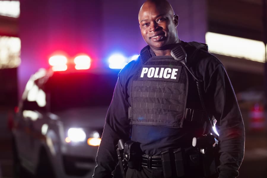 Smiling police officer standing in front of police car