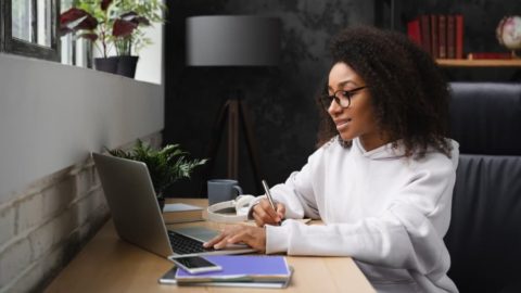 Student taking online course sitting at table with laptop and notebooks