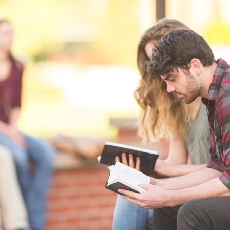 Two college students reading Bible together on park bench outside